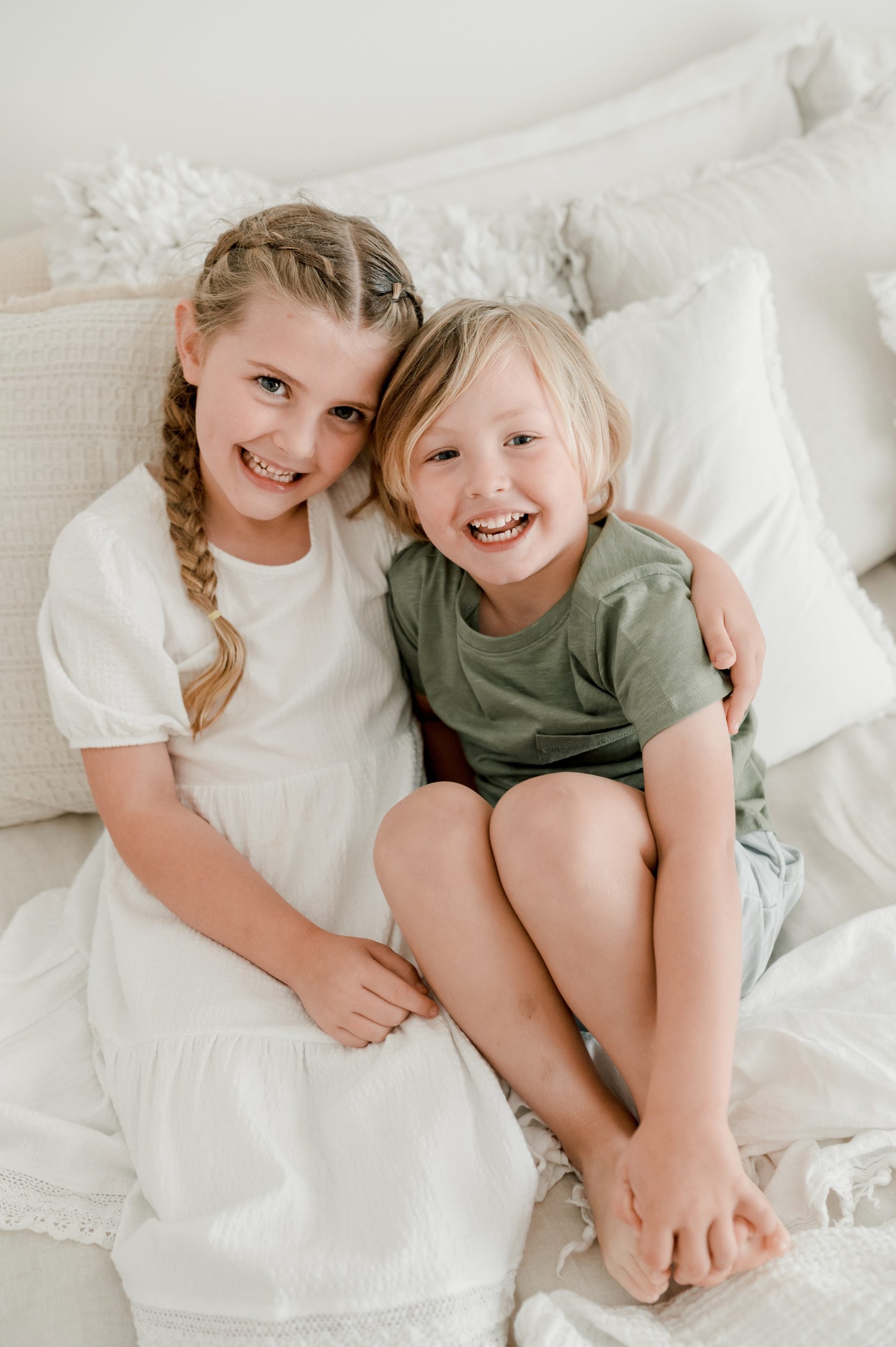 The lovely Jake & Freya are photographed in Kate & Co's natural light studio in Edwardstown, South Australia. They wear neutral colours and are laying back in soft cusions on a white linen bed. Their big beautiful smiles look straight up to camera.