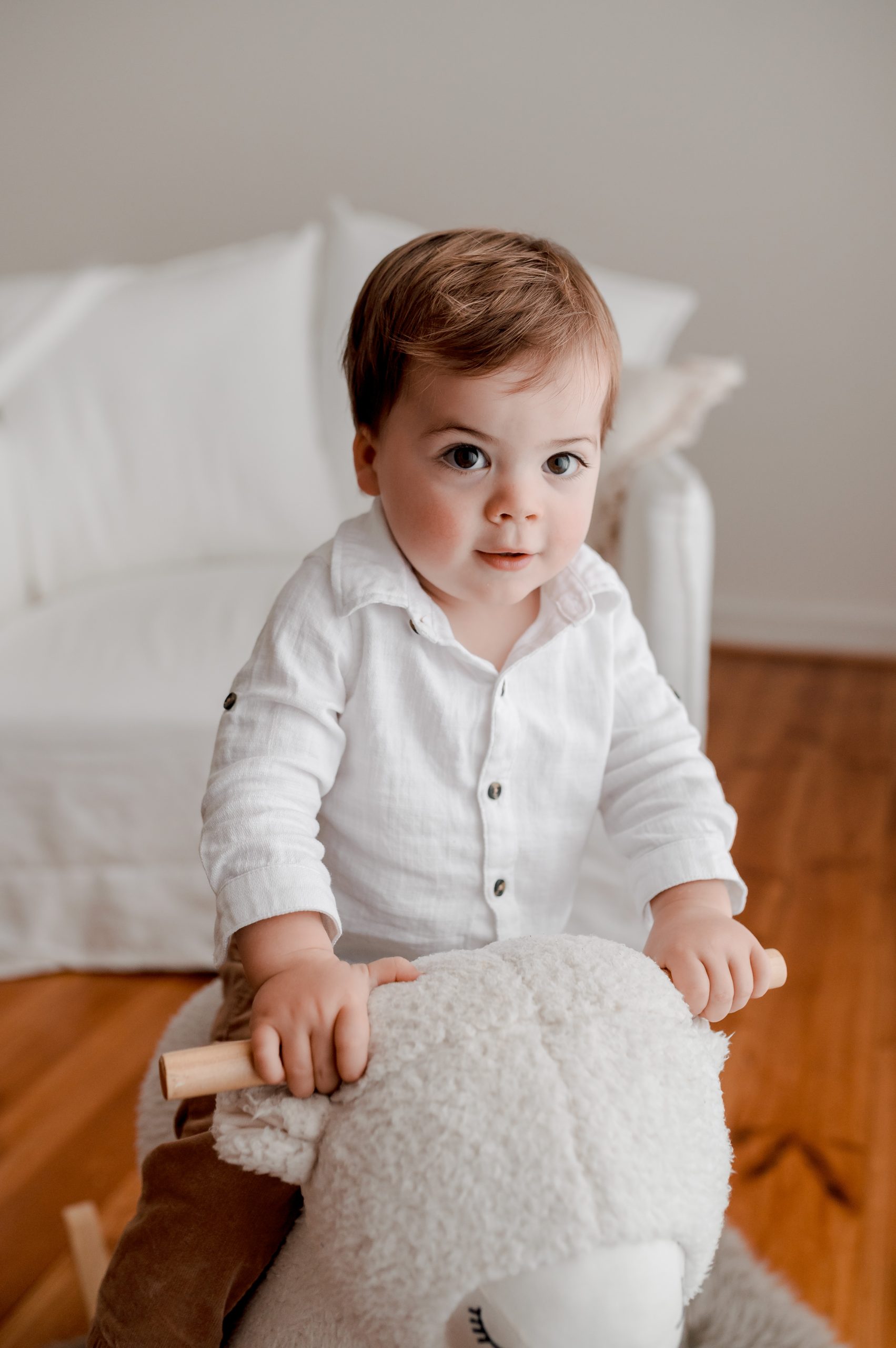 Baby Isaac is nearly 12 months old, he is photographed on a white rocking horse and we wears a white shirt. His big eyes are bright in the lovely natural filtered light.