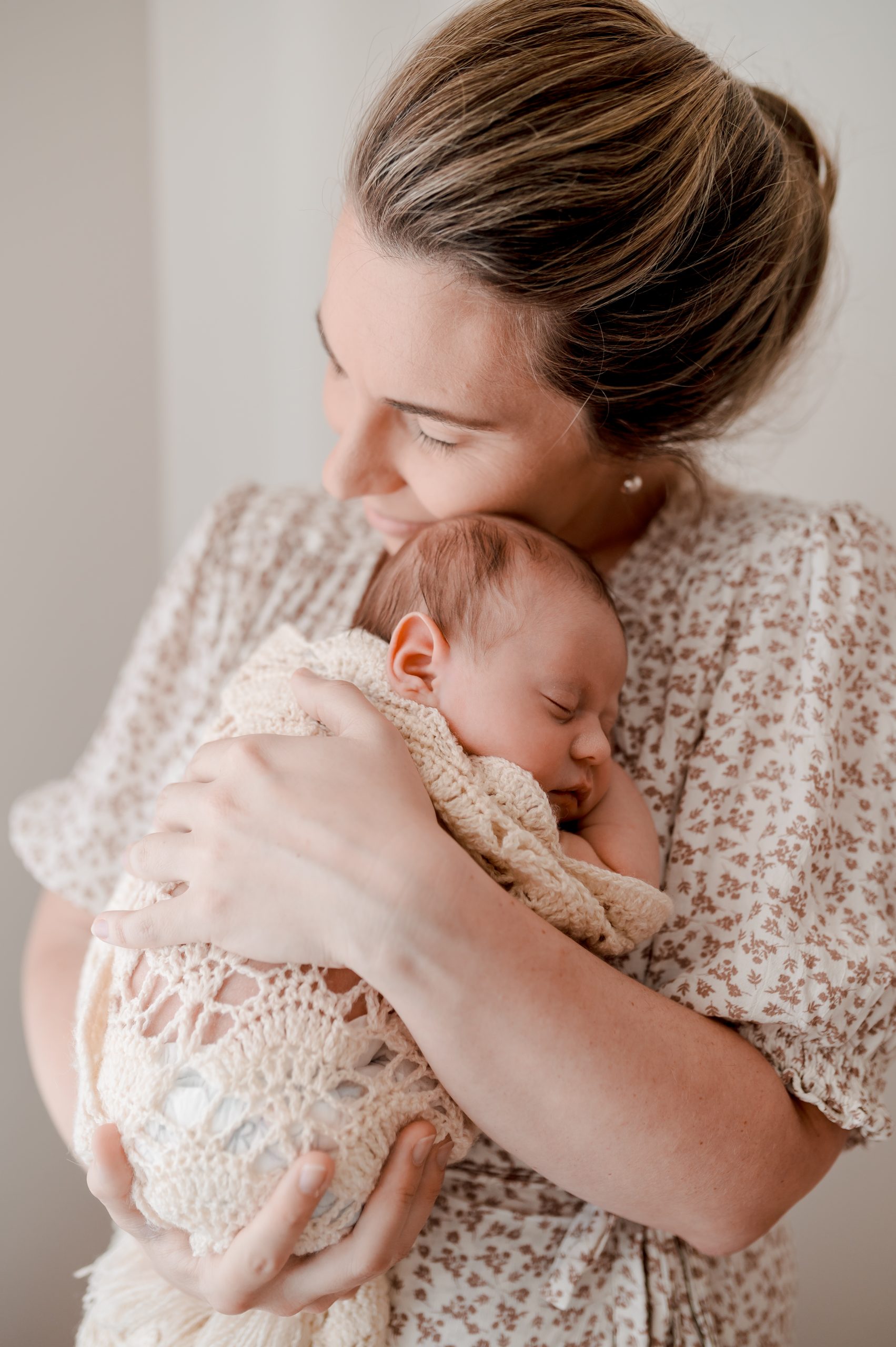 beautiful elegant mother holding her newborn baby to her chest in a loving embrace with beautiful light and neutral tones