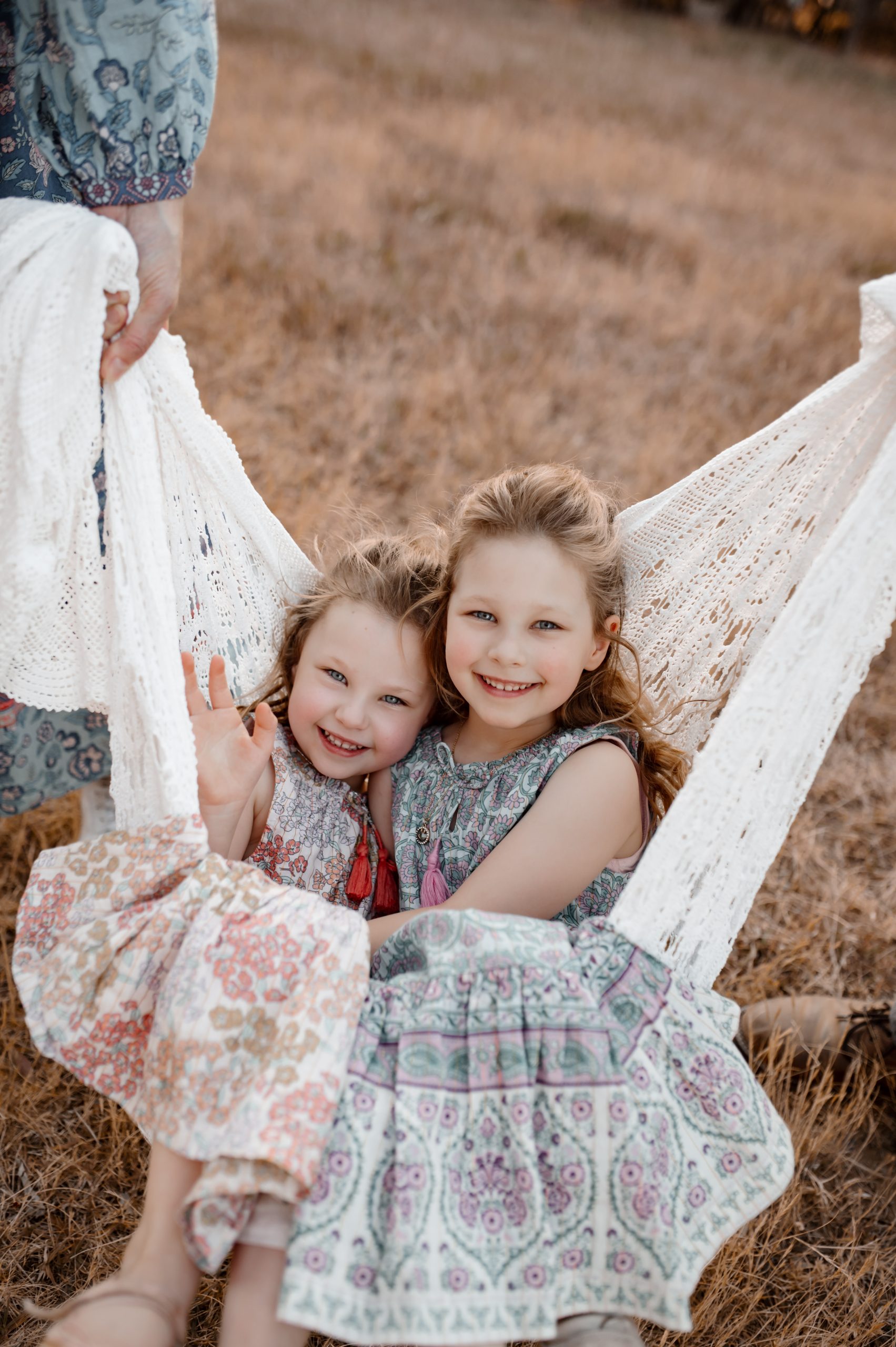 twin girls swinging in a hammock held by their parents, they are smiling and looking at the camera and having fun